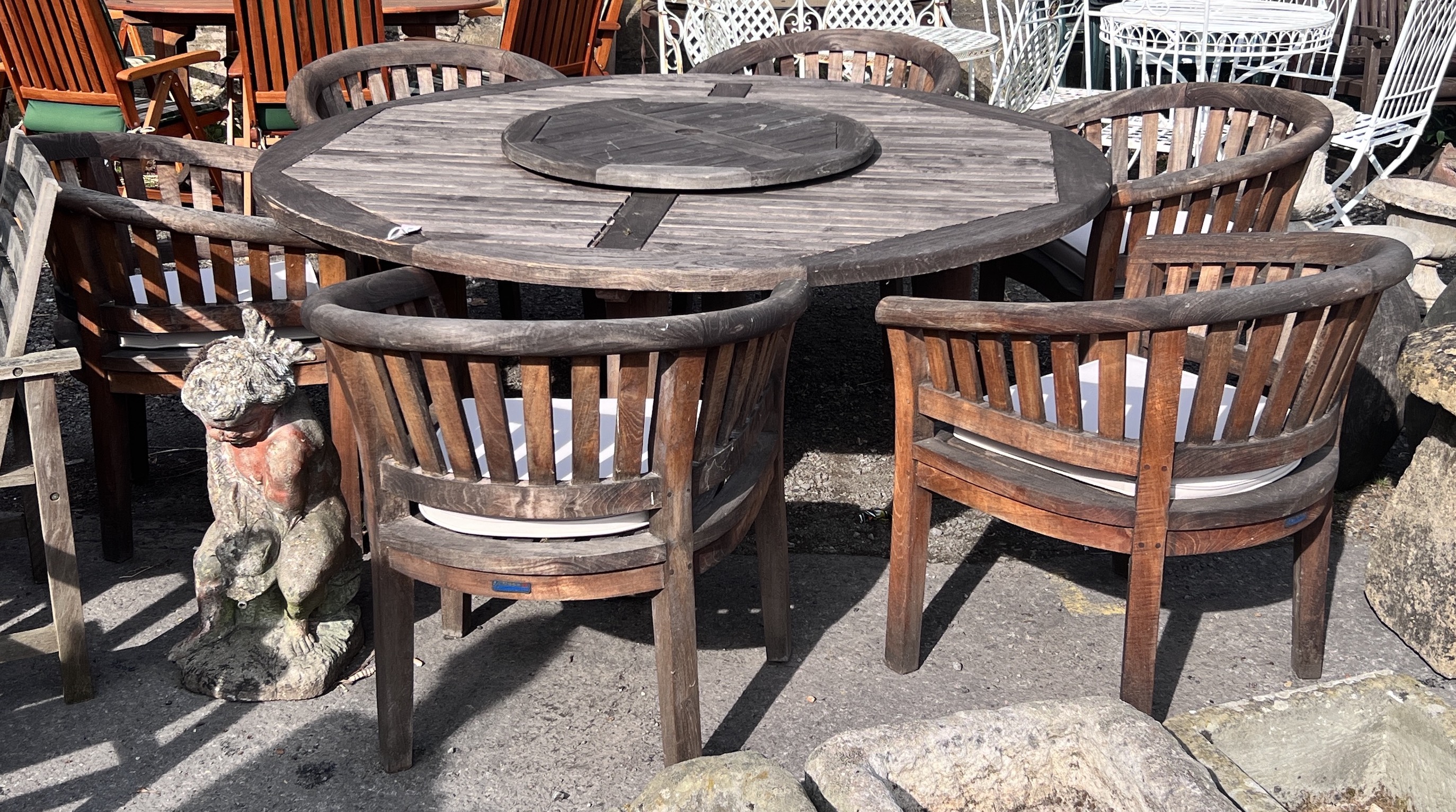A large circular weathered teak garden table with Lazy Susan, diameter 180cm, height 75cm, together with six tub framed chairs with seat cushions